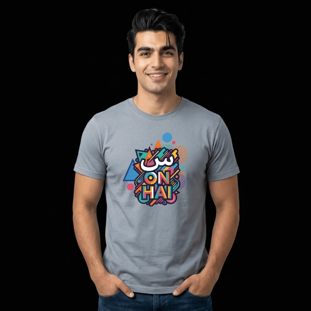 A man wearing a light gray crewneck t-shirt with a colorful graphic print on the chest that reads 'SCENE ON HAI'. The background is solid black.